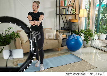 Mature fitness blogger filming herself warming up before training at home 94334370