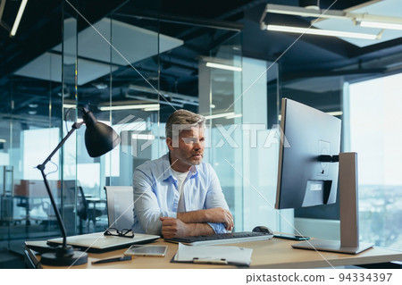 Business man in thought, solves important issues, and makes choices, gray-haired businessman works at computer in modern office 94334397