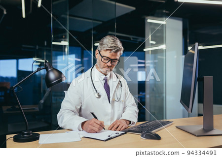 An experienced doctor works in a modern computer clinic, a gray-haired man works remotely, provides advice to patients online An experienced doctor works in a modern computer clinic, a gray-haired man works remotely, provides advice to patients online 94334491
