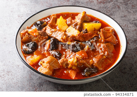 Khoresht Aloo Stewed lamb meat with dried plums or prunes, tomato, onion, potato, carrot and garlic closeup in the bowl. Horizontal 94334871