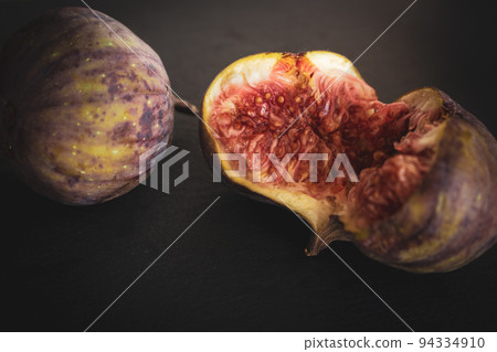 Figs on black background. Fresh juicy fruits. Ripe exotic fruit. Purple cracked fig. Raw dessert. Fig close up. Seasonal fruit. Autumn harvest. 94334910