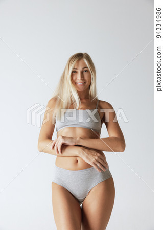 Young pretty slim 35 years old woman in cotton inner wear isolated over gray studio background. Wellness, wellbeing, fitness, diet, natural beauty of female body Young pretty slim 35 years old woman in cotton inner wear isolated over gray studio background. Wellness, wellbeing, fitness, diet, natural beauty of female body 94334986
