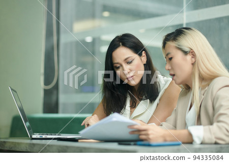 Serious female entrepreneurs working on project together, analyzing data and statistics in papers and 94335084