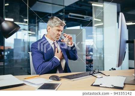 Gray-haired businessman has a severe chest pain, an experienced worker working at a desk in the office Gray-haired businessman has a severe chest pain, an experienced worker working at a desk in the office 94335142