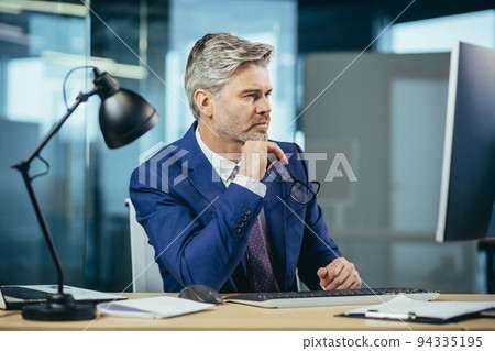 Portrait of a man, businessman thinking while working in the office at the computer Portrait of a man, businessman thinking while working in the office at the computer 94335195