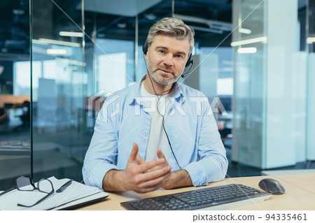 Experienced and successful businessman, looks at the webcam and smiles, talks to colleagues, online meeting, works in a modern office and uses a headset, video call Experienced and successful businessman, looks at the webcam and smiles, talks to colleagues, online meeting, works in a modern office and uses a headset, video call 94335461