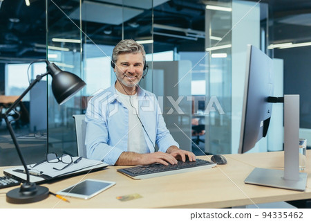 Portrait of a successful businessman, gray-haired man talking to colleagues on a video call, using a headset, smiling and rejoicing Portrait of a successful businessman, gray-haired man talking to colleagues on a video call, using a headset, smiling and rejoicing 94335462