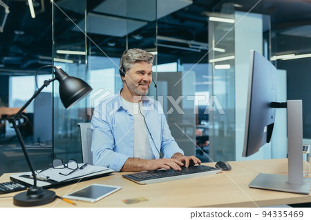 Portrait of a successful businessman, gray-haired man talking to colleagues on a video call, using a headset, smiling and rejoicing 94335469