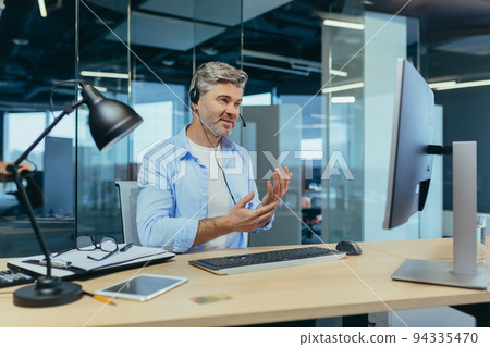 Senior and experienced employee, advises the buyer on a video call, the man works in a modern office uses webcam 94335470