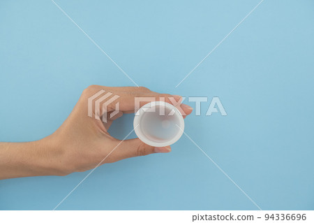 Close-up of a woman's hand holding a menstrual cup against a blue background. Women's health concept, zero waste alternatives Close-up of a woman's hand holding a menstrual cup against a blue background. Women's health concept, zero waste alternatives 94336696