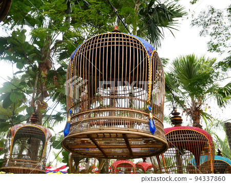 MELAKA, MALAYSIA -JUNE 7, 2022: Traditional bird cages made of bamboo are hung in an open area. Has a fabric cover to protect the bird inside from the weather. Displayed for exhibition. MELAKA, MALAYSIA -JUNE 7, 2022: Traditional bird cages made of bamboo are hung in an open area. Has a fabric cover to protect the bird inside from the weather. Displayed for exhibition. 94337860