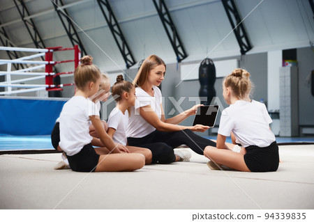 Coaching. Beginner gymnastics athletes doing exercises with gymnastics equipment at sports gym, indoors. Concept of sport, studying, art, education 94339835