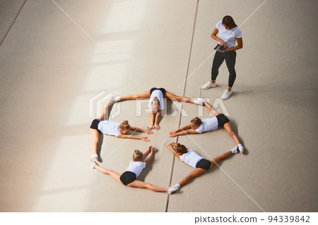 Aerial view. Female sports coach training gymnastics athletes at sports gym, indoors. Concept of sport, studying, art, education Aerial view. Female sports coach training gymnastics athletes at sports gym, indoors. Concept of sport, studying, art, education 94339842