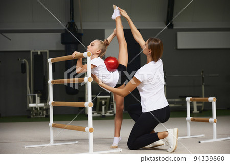 Sport training with coach. Preparing for sport competition. Beginner gymnastics athletes doing exercises with gymnastics equipment at sports gym, indoors. 94339860