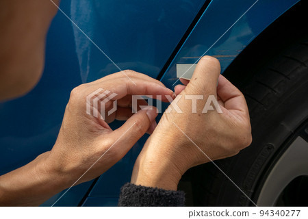 Senior man's hand trying to repair scratches on the body of a blue car Senior man's hand trying to repair scratches on the body of a blue car 94340277