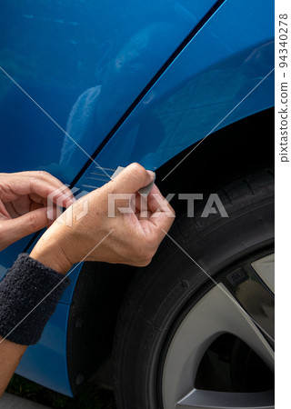 Senior man's hand trying to repair scratches on the body of a blue car 94340278