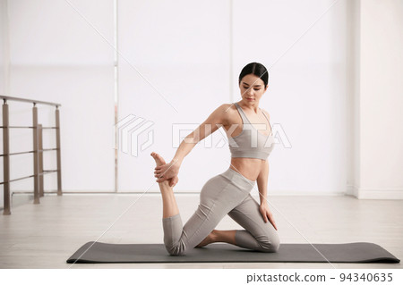 Young woman practicing One Legged King Pigeon asana in yoga studio. Eka Pada Rajakapotasana pose 94340635