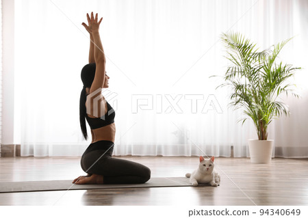 Young woman practicing thunderbolt asana with cat in yoga studio. Vajrasana pose 94340649
