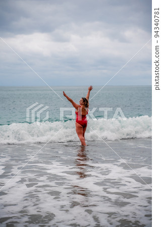Woman in a bathing suit at the sea. A fat young woman in a red swimsuit enters the water during the surf 94340781