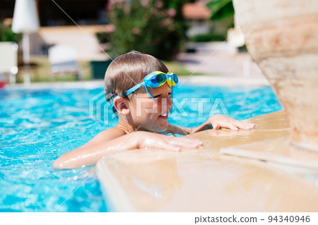 Boy with swimming goggles is resting after swimming in the pool. Boy with swimming goggles is resting after swimming in the pool. 94340946