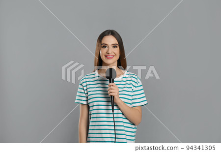 Young female journalist with microphone on grey background Young female journalist with microphone on grey background 94341305