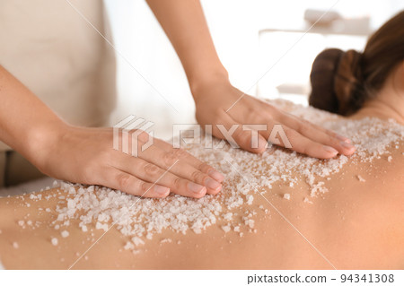 Young woman having body scrubbing procedure with sea salt in spa salon, closeup Young woman having body scrubbing procedure with sea salt in spa salon, closeup 94341308
