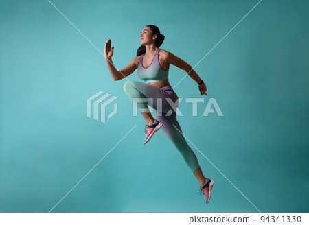 Athletic young woman running on turquoise background, side view Athletic young woman running on turquoise background, side view 94341330