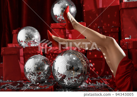 Woman sitting near disco balls on red Christmas gifts indoors, closeup 94343005