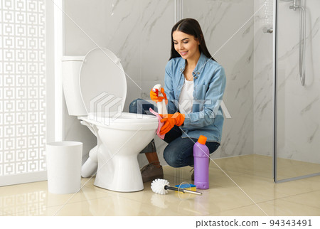 Young woman cleaning toilet bowl in bathroom Young woman cleaning toilet bowl in bathroom 94343491