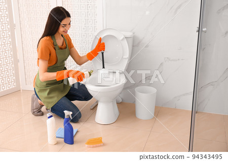 Young woman cleaning toilet bowl in bathroom Young woman cleaning toilet bowl in bathroom 94343495