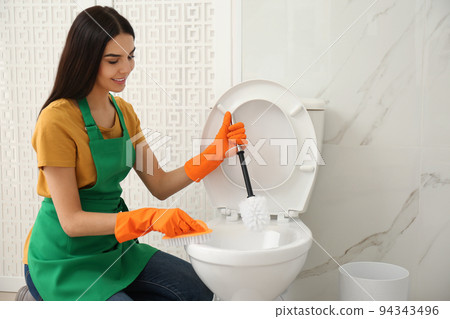 Young woman cleaning toilet bowl in bathroom Young woman cleaning toilet bowl in bathroom 94343496