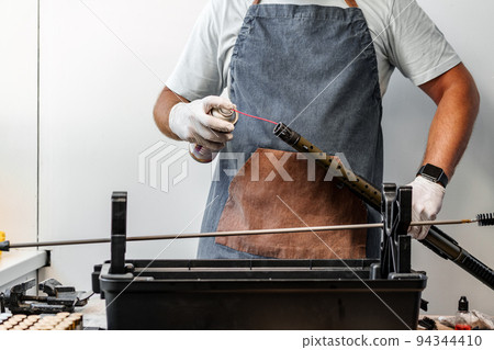 Close up of a man in apron lubricates the mechanism of the weapon with oil 94344410