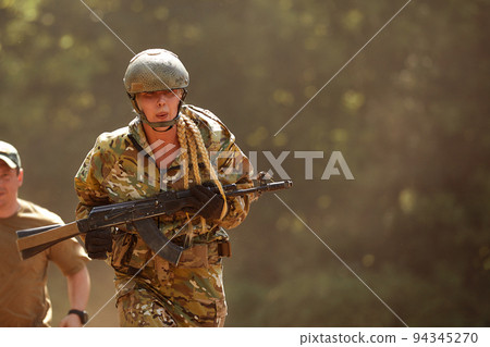 Portrait of fit military female holding weapon rifle in hands in river, posing alone. Confident strong athlete lady looking at side seriously. Attractive good-looking female in military gear 94345270