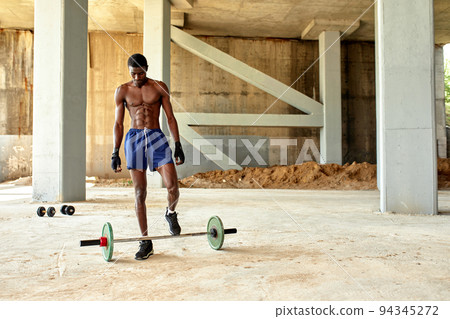 Athletic black young man lifting a heavy-weight barbell in outdoor gym under the bridge. Healthy lifestyle concept Athletic black young man lifting a heavy-weight barbell in outdoor gym under the bridge. Healthy lifestyle concept 94345272