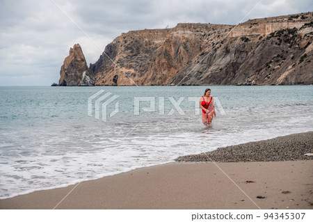 Woman in a bathing suit at the sea. A fat young woman in a red swimsuit enters the water during the surf Woman in a bathing suit at the sea. A fat young woman in a red swimsuit enters the water during the surf 94345307