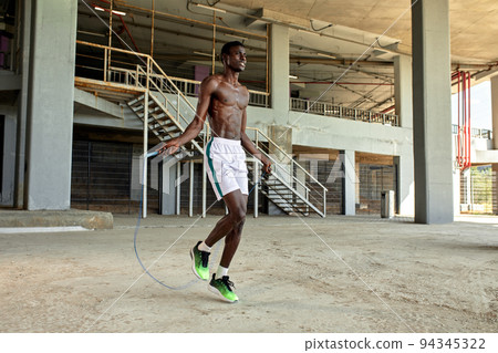 Black young sportsman working out with jumping rope outdoors 94345322