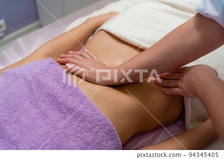 Top view of hands massaging female abdomen.Therapist applying pressure on belly. Woman receiving massage at spa salon 94345405