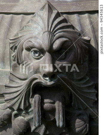 Demonic statue face made of metal on a street lamp 94345613