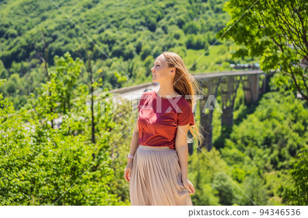 Montenegro. Woman tourist in background of Dzhurdzhevich Bridge Over The River Tara. Travel around Montenegro concept. Sights of Montenegro Portrait of a disgruntled girl sitting at a cafe table 94346536
