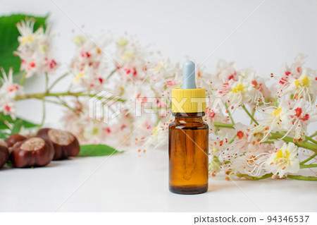 Bottle of horse chestnut extract, essence of chestnut flowers. Flowering branches and leaves of horse chestnut. 94346537
