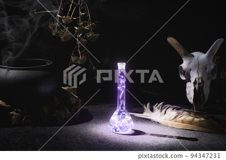 Witchcraft or alchemistry altar. Goats skull, flask with glowing plasma, falcon feather, dry herbs, iron cauldron, smoking incense in the dark, low key, selective focus. Witchcraft or alchemistry altar. Goats skull, flask with glowing plasma, falcon feather, dry herbs, iron cauldron, smoking incense in the dark, low key, selective focus. 94347231