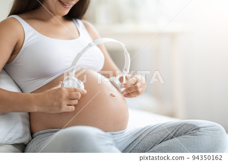 Cropped of expecting lady holding headphones on her big belly 94350162