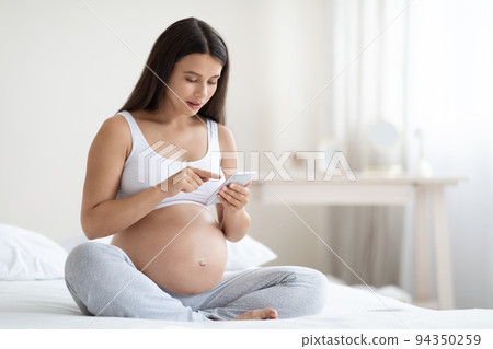 Peaceful expecting lady using cell phone, bedroom interior Peaceful expecting lady using cell phone, bedroom interior 94350259