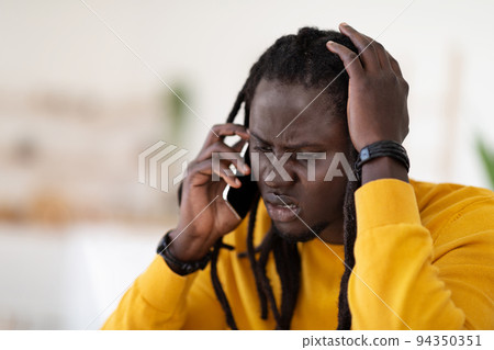 Confused Young Black Guy Talking On Cellphone And Touching Head Confused Young Black Guy Talking On Cellphone And Touching Head 94350351