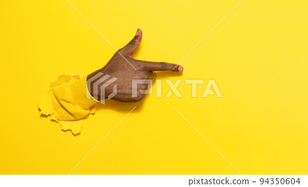 African american male hand pointing aside on virtual object or text, gesturing through the torn yellow paper background African american male hand pointing aside on virtual object or text, gesturing through the torn yellow paper background 94350604