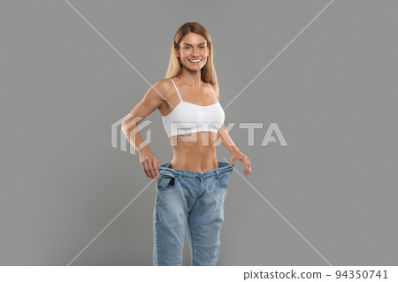 Beautiful Slim Woman In Oversized Jeans Standing Over Grey Studio Background 94350741