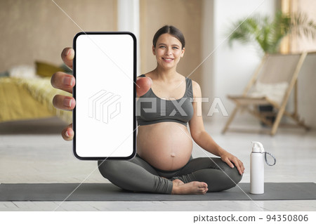 Happy Young Pregnant Woman Practicing Yoga At Home And Demonstrating Blank Smartphone Happy Young Pregnant Woman Practicing Yoga At Home And Demonstrating Blank Smartphone 94350806