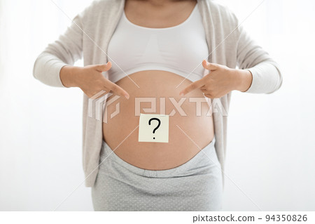 Expecting lady showing paper sticker with question mark on tummy 94350826