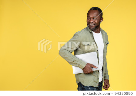 Smiling confident mature black male in casual, wireless headphones with laptop looking back at empty space 94350890