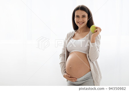 Cheerful pregnant lady holding green apple and smiling 94350982